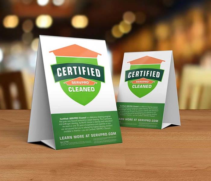 Table tent signs describing the Certified: SERVPRO Cleaned program on top of a wooden table.